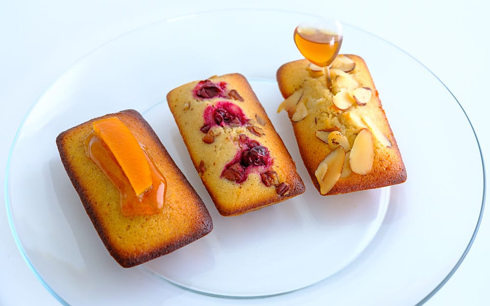 Three financiers — almond, cranberry-pecan, and orange with honey — on a glass plate